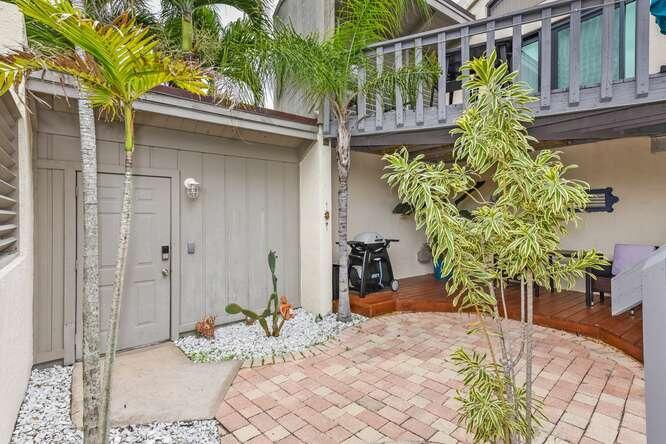 A patio area features a gray door, a grill, a palm tree, and brick pavers — 1605 S Us Highway 1 # 9h, Jupiter FL 33477, JUPITER, FL