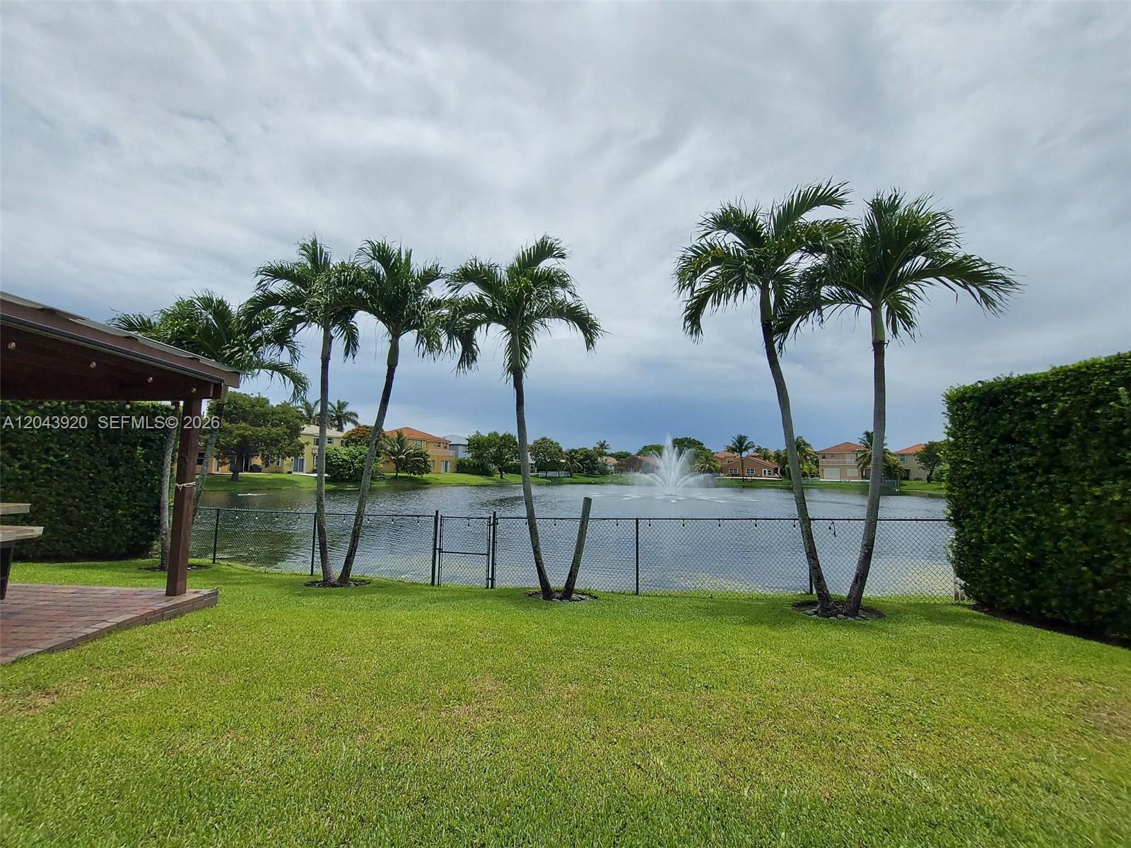 A backyard lawn features a chain-link fence, palm trees, and a pond with a fountain — 5350 SW 130th Ter # 5350, Miramar FL 33027, MIRAMAR, FL