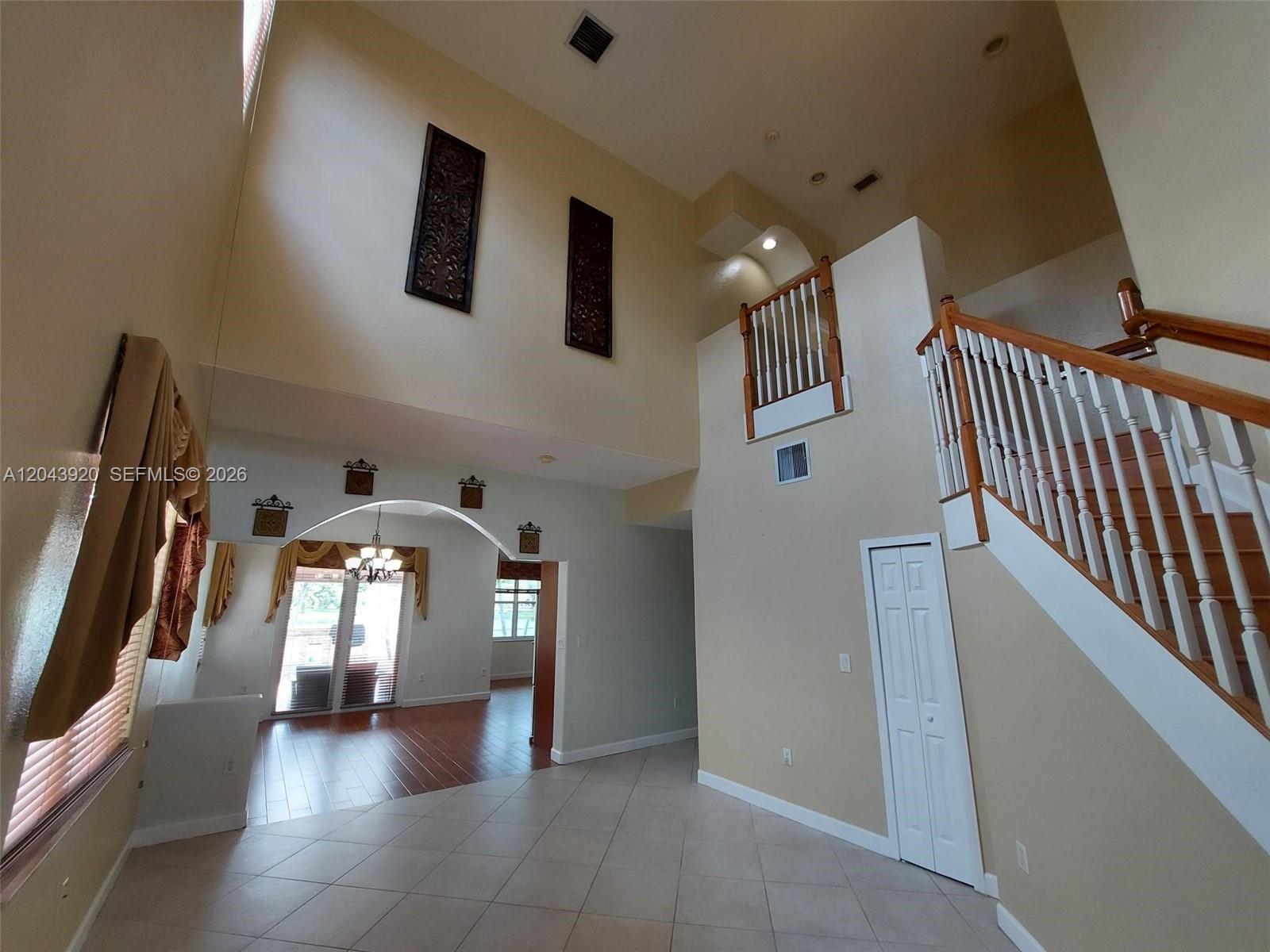 A high-ceilinged foyer features tile flooring, a staircase with wooden railings, and an arched entryway — 5350 SW 130th Ter # 5350, Miramar FL 33027, MIRAMAR, FL