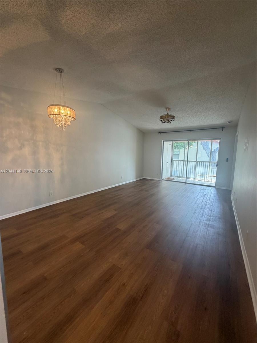 An empty living room features wood-look flooring, a crystal chandelier, and a sliding glass door — 3031 Holiday Springs Blvd # 7, Margate FL 33063, MARGATE, FL