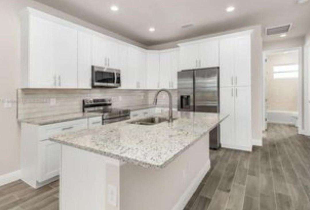 A modern kitchen features white cabinets, granite countertops, stainless steel appliances, and wood-look tile flooring — 321 Neighborly Road, FL 33935, FL