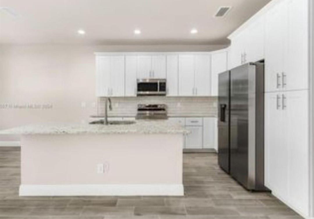 A modern kitchen features white cabinets, stainless steel appliances, and a granite-topped island — 321 Neighborly Road, FL 33935, FL