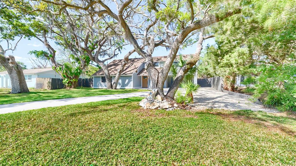 A house with a light-colored exterior and a gravel driveway sits behind large oak trees — 7331 DIANNE DRIVE, NEW PORT RICHEY, FL