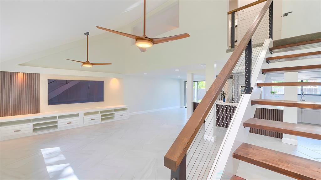 A modern living room features a floating staircase, wood-paneled accent wall, and two ceiling fans — 7331 DIANNE DRIVE, NEW PORT RICHEY, FL