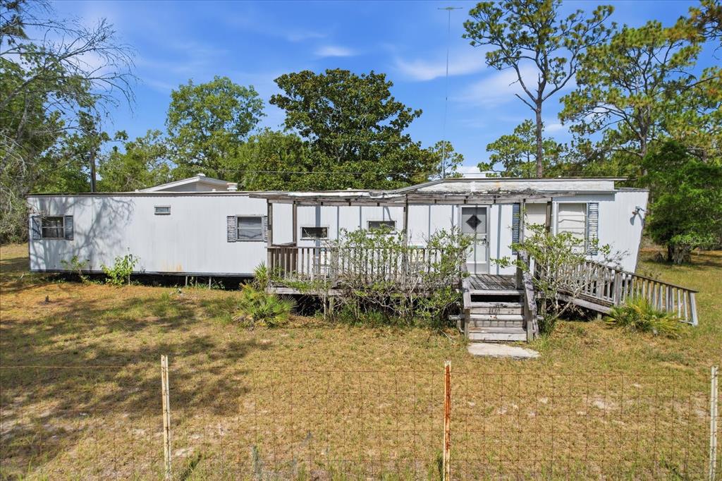An exterior view of a weathered mobile home featuring a wooden deck and porch — 4675 W ROSES COURT, HOMOSASSA, FL