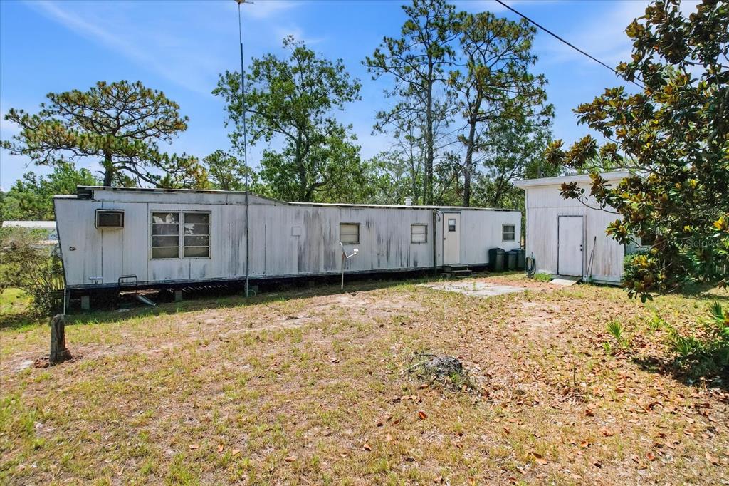 A weathered mobile home with an attached shed sits on a grassy, wooded lot — 4675 W ROSES COURT, HOMOSASSA, FL