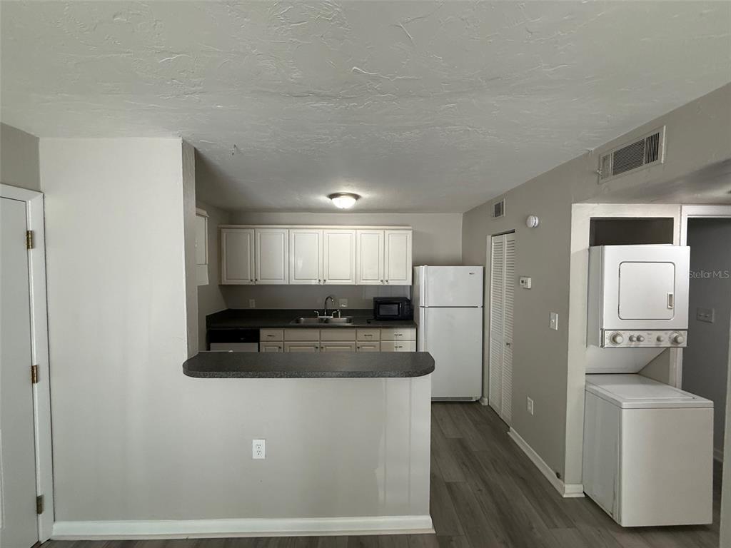 A kitchen features white cabinets, dark countertops, a white refrigerator, and an adjacent laundry area — 1035 SW 9TH STREET UNIT 1, GAINESVILLE, FL