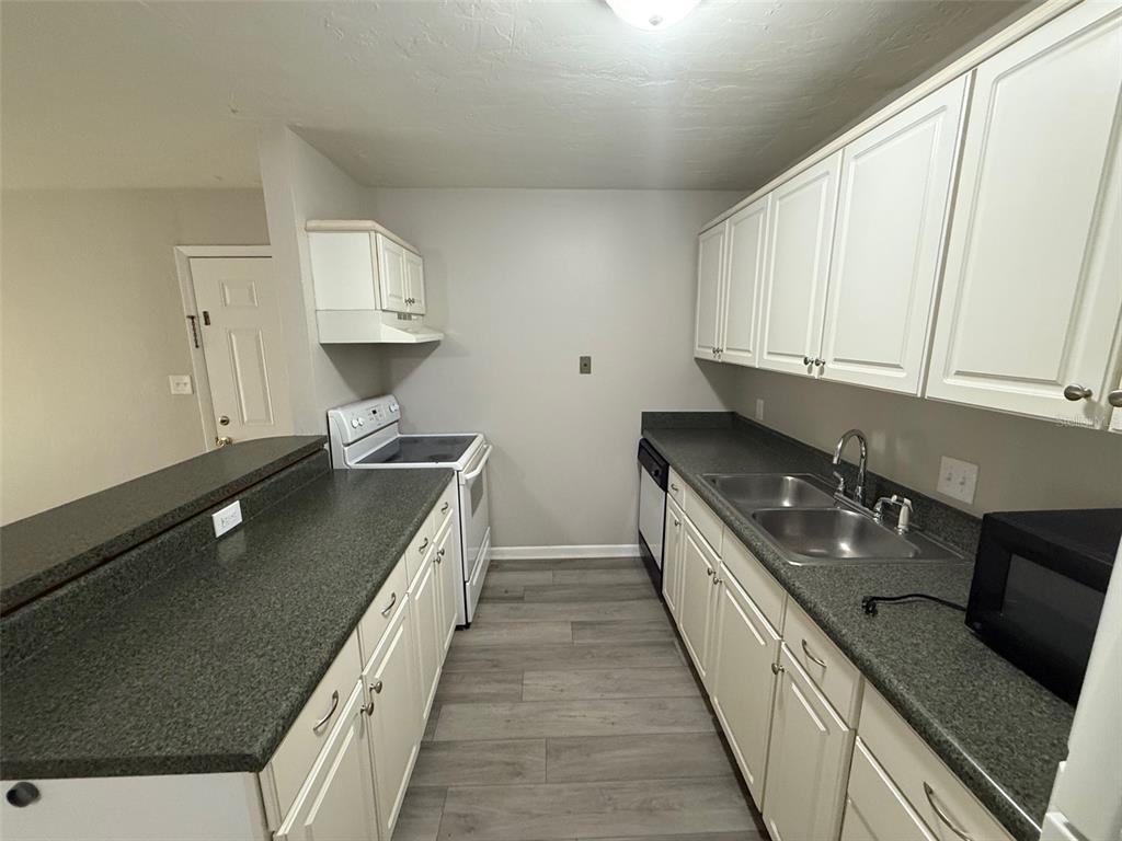 A galley kitchen features white cabinets, dark gray countertops, and light wood-look flooring — 1035 SW 9TH STREET UNIT 1, GAINESVILLE, FL