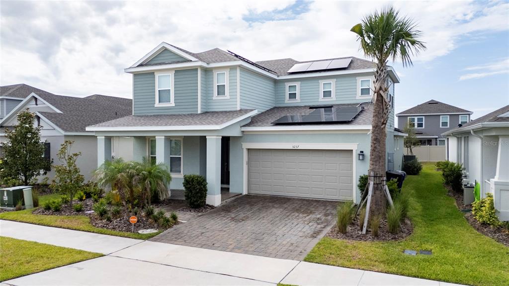 A two-story house with light blue siding, a paved driveway, and solar panels on the roof — 5237 STONE RIDGE PLACE, ST CLOUD, FL