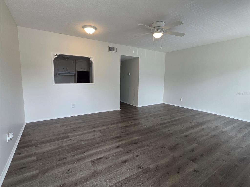 An empty living room features gray wood-look flooring, white walls, and a ceiling fan — 2459 COLUMBIA DRIVE UNIT 47, CLEARWATER, FL