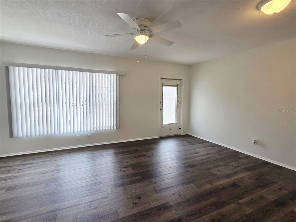 An empty room features dark wood-look flooring, a ceiling fan, vertical blinds, and a door — 2459 COLUMBIA DRIVE UNIT 47, CLEARWATER, FL