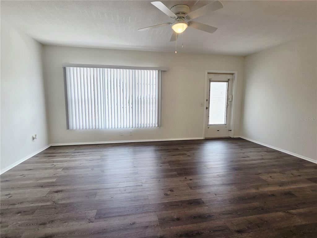 An empty room features wood-look flooring, a ceiling fan, vertical blinds, and a glass-paneled door — 2459 COLUMBIA DRIVE UNIT 47, CLEARWATER, FL