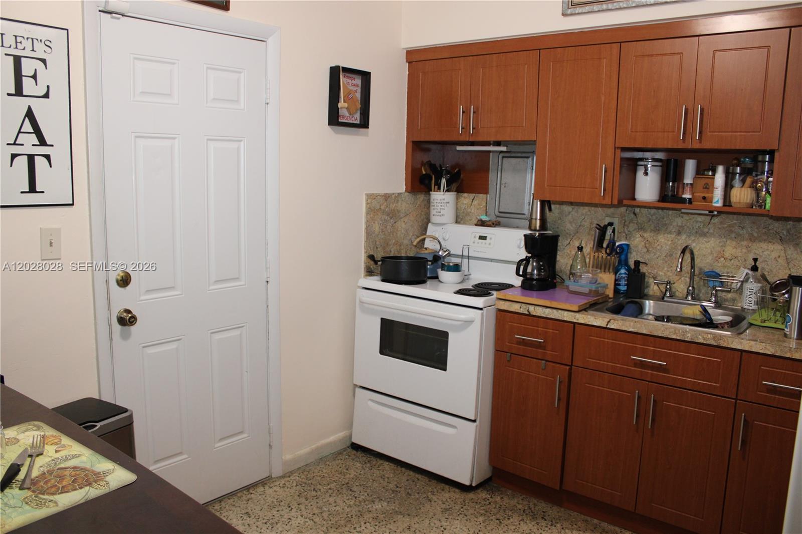 A kitchen features wood cabinets, a white stove, a sink, and a white door — 1022 NW 22nd Pl, Miami FL 33125, MIAMI, FL