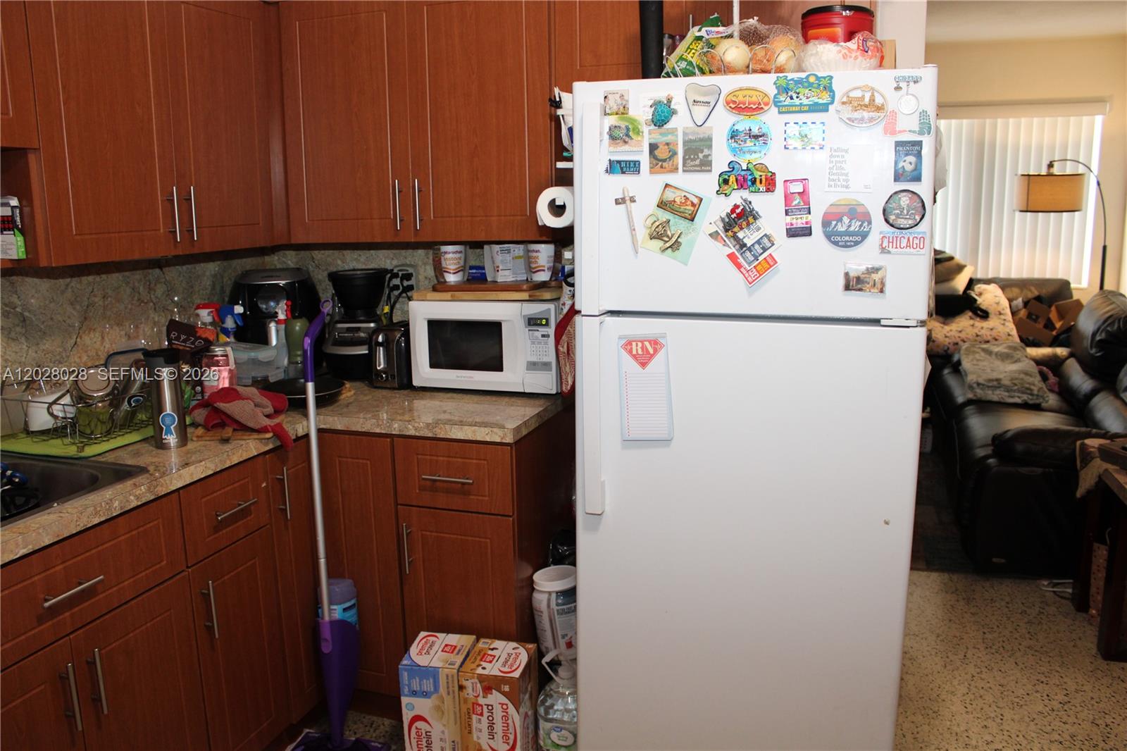A kitchen features wood cabinets, a white refrigerator covered in magnets, and a microwave — 1022 NW 22nd Pl, Miami FL 33125, MIAMI, FL