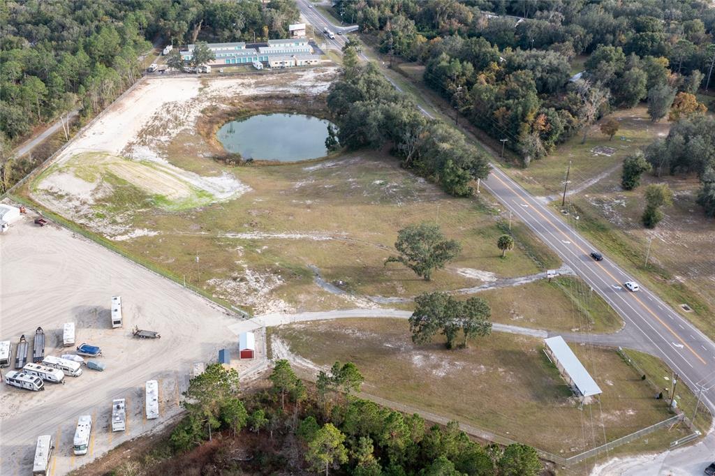 An aerial view shows a vacant lot with a pond, trees, and adjacent storage facility — 1177 SE KEYSTONE AVENUE, KEYSTONE HEIGHTS, FL