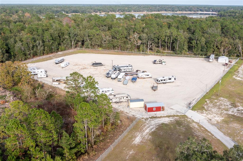 An aerial view shows a fenced gravel lot containing multiple parked recreational vehicles and sheds — 1177 SE KEYSTONE AVENUE, KEYSTONE HEIGHTS, FL