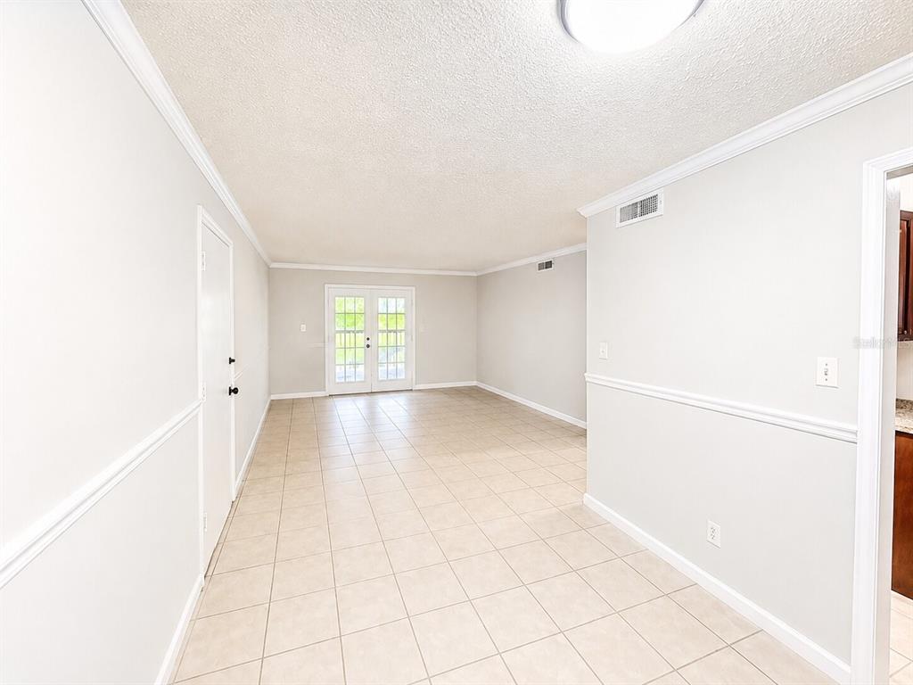 An empty room with light-colored tile flooring, white walls, chair rail molding, and French doors — 405 WYMORE ROAD UNIT 106, ALTAMONTE SPRINGS, FL