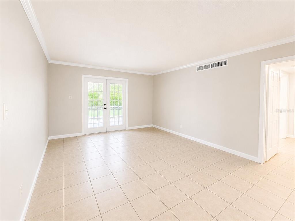 An empty room with beige tile flooring, light-colored walls, and white French doors — 405 WYMORE ROAD UNIT 106, ALTAMONTE SPRINGS, FL