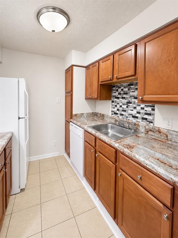 A kitchen features wood cabinets, granite countertops, a mosaic tile backsplash, and a white refrigerator — 405 WYMORE ROAD UNIT 106, ALTAMONTE SPRINGS, FL