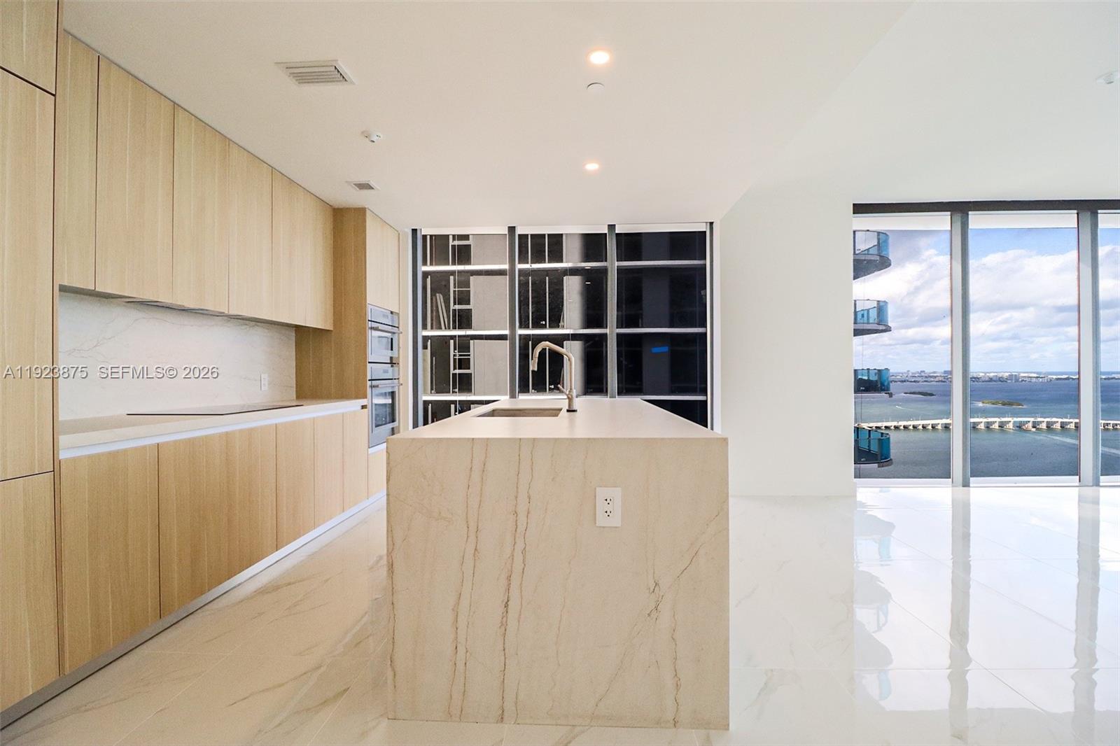 A modern kitchen features light wood cabinetry, a stone island, and floor-to-ceiling windows with water views — 700 NE 24 st # 4201, Miami FL 33137, MIAMI, FL