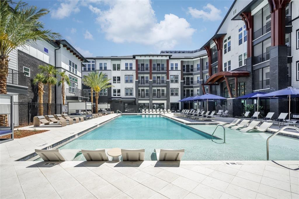 A large rectangular swimming pool with lounge chairs sits in a courtyard between apartment buildings — 20191 SABAL PALM COURT UNIT A1.1, LAND O LAKES, FL