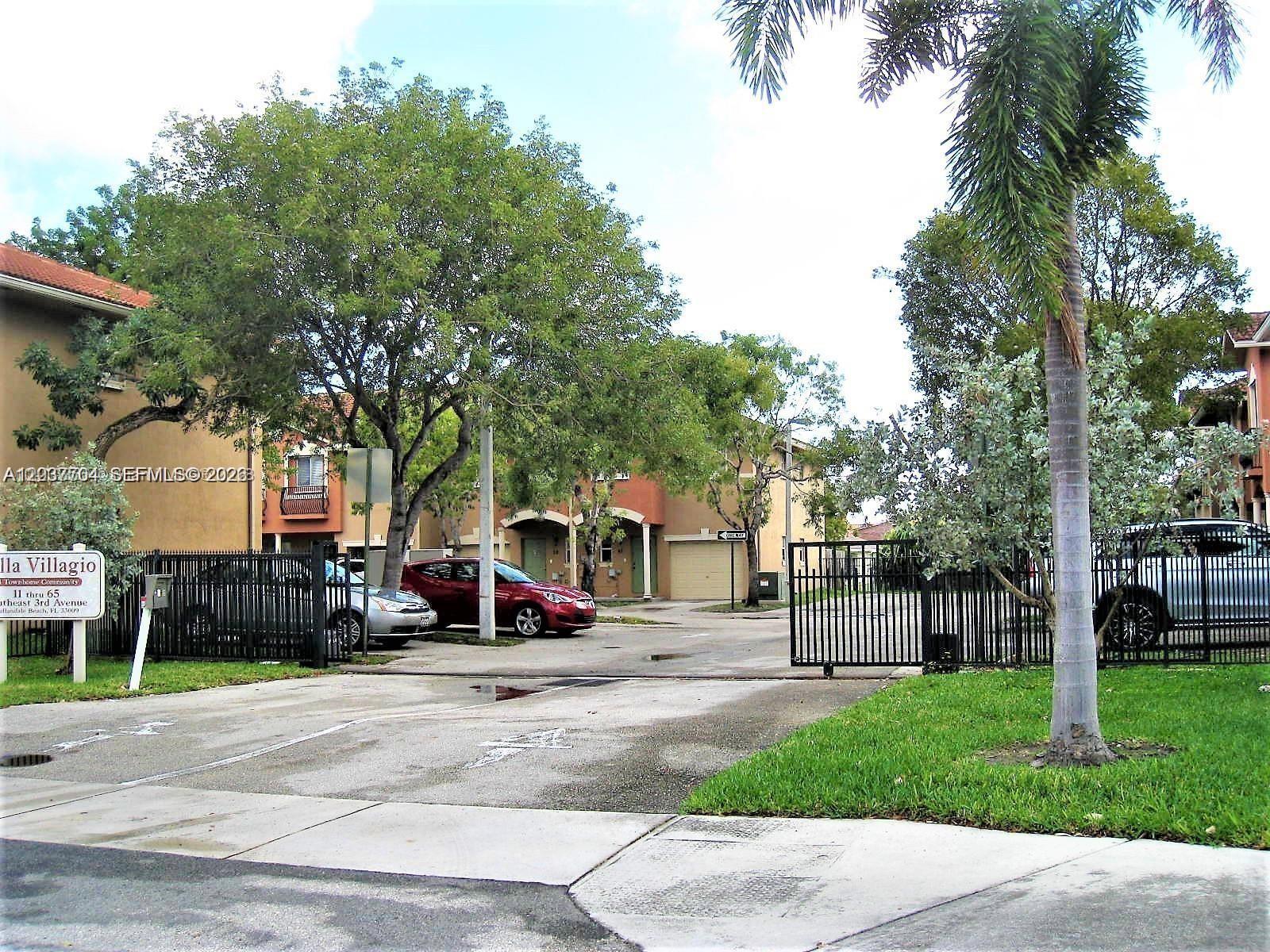 A gated entrance leads to a residential complex with townhomes, trees, and parked cars — 33 SE 3rd Ave, Hallandale Beach FL 33009, HALLANDALE BEACH, FL