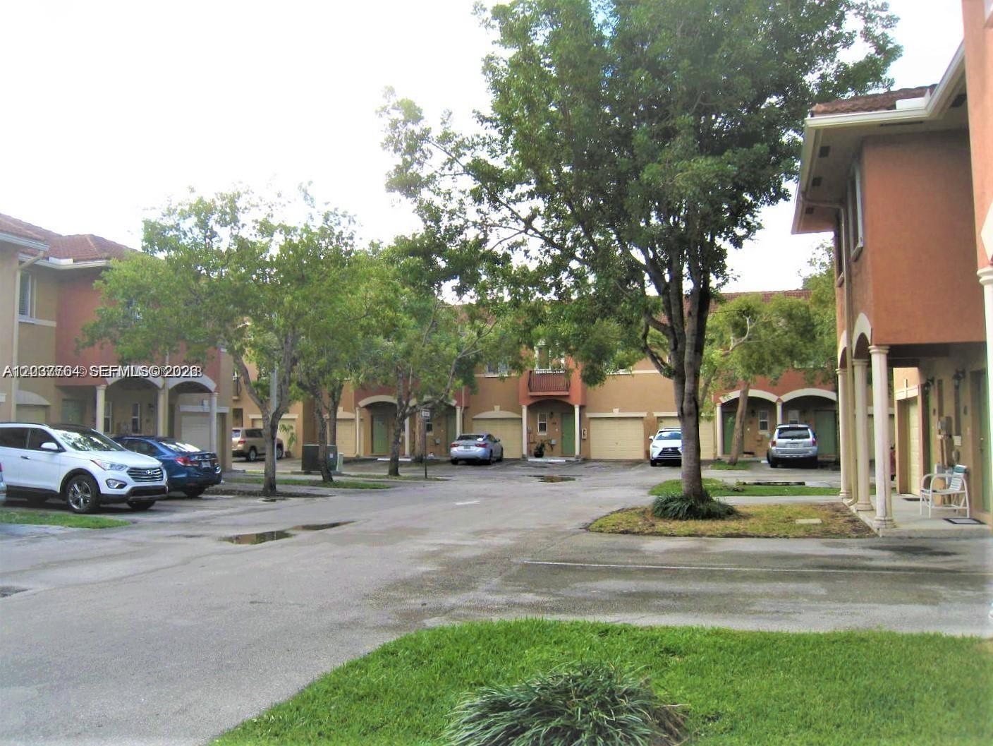 A view of a residential townhouse complex with parked cars and mature trees — 33 SE 3rd Ave, Hallandale Beach FL 33009, HALLANDALE BEACH, FL