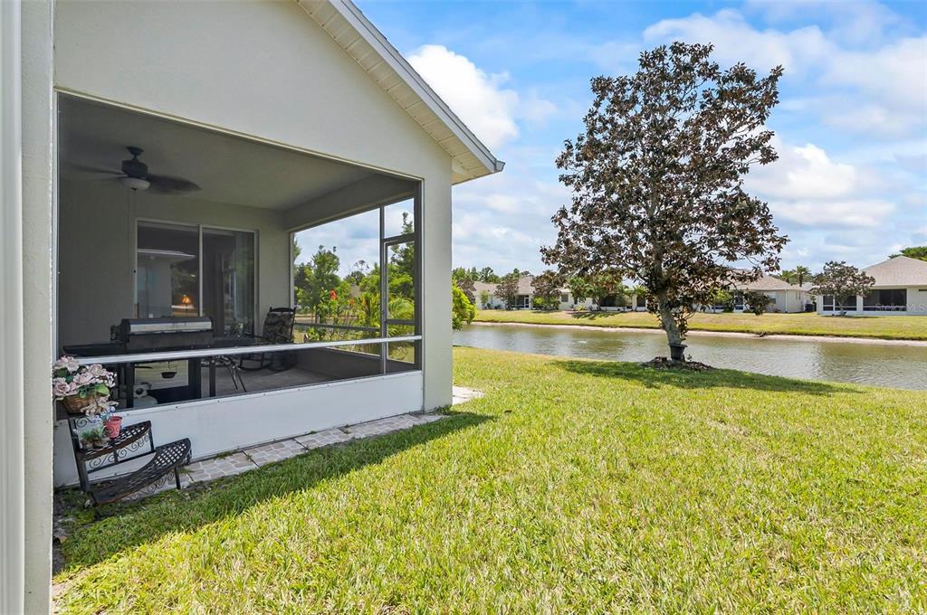 A screened-in patio overlooks a grassy lawn and a pond with houses in the distance — 19 RAINTREE CIRCLE, PALM COAST, FL
