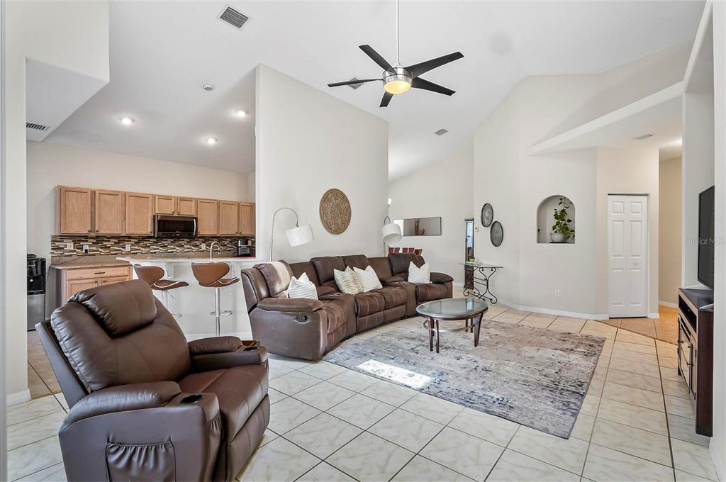 A living room with tile floors, a brown sectional, a recliner, and an open kitchen — 19 RAINTREE CIRCLE, PALM COAST, FL
