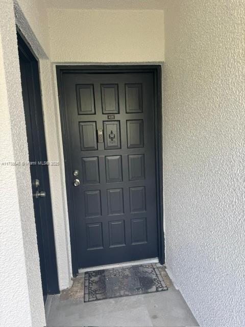 A dark-colored front door with a door knocker is set into a textured white wall — 3301 Spanish Moss Ter # 415, Lauderhill FL 33319, LAUDERHILL, FL