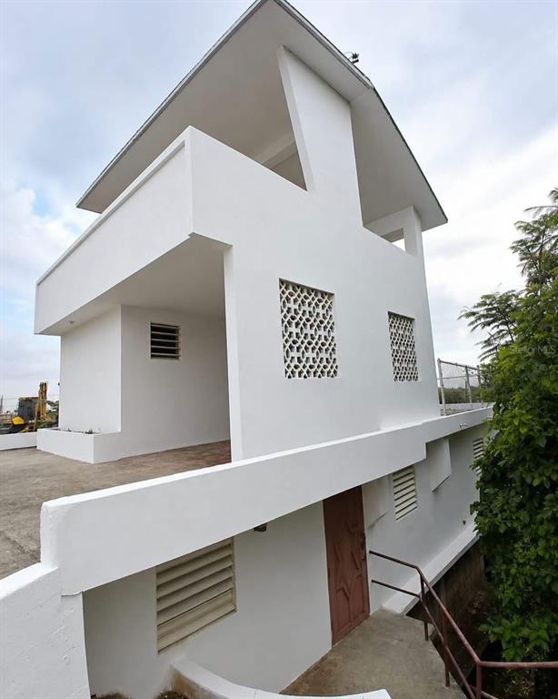 A white, multi-level modern house features geometric breeze block screens and a brown front door — PR-2 Km 90.2 BO PUENTE, CAMUY, PR