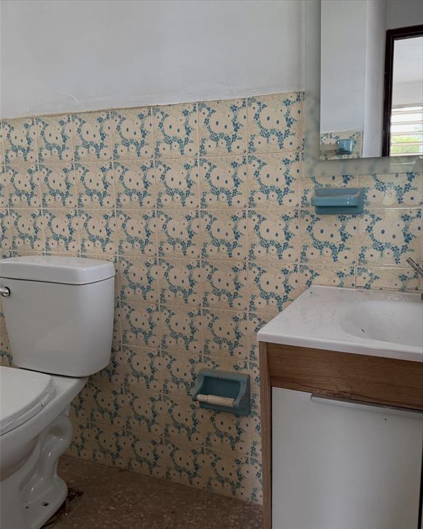 A bathroom features a white toilet, a modern vanity, and vintage floral-patterned wall tiles — PR-2 Km 90.2 BO PUENTE, CAMUY, PR