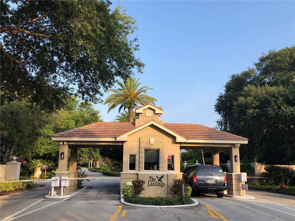 A gated entrance with a guardhouse and a vehicle passing through under a tiled roof — 1664 STARLING DRIVE UNIT 101, SARASOTA, FL