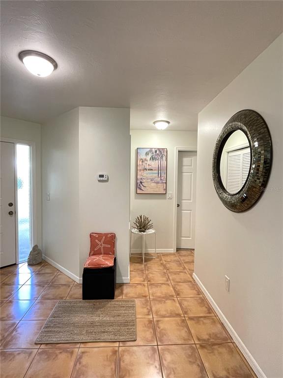 An entryway features tile flooring, a round mirror, a small stool, and a wall painting — 1664 STARLING DRIVE UNIT 101, SARASOTA, FL