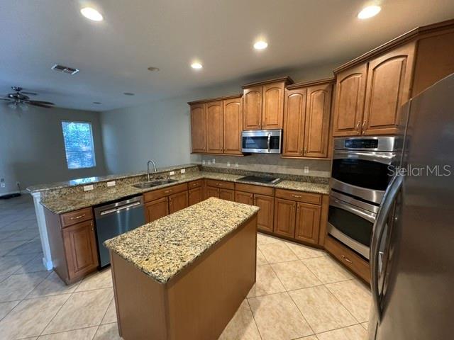 A kitchen features wood cabinets, granite countertops, a center island, and stainless steel appliances — 1079 GLENRAVEN LANE, CLERMONT, FL