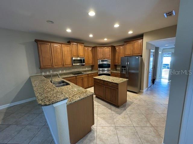 A kitchen features wood cabinets, granite countertops, a center island, and stainless steel appliances — 1079 GLENRAVEN LANE, CLERMONT, FL
