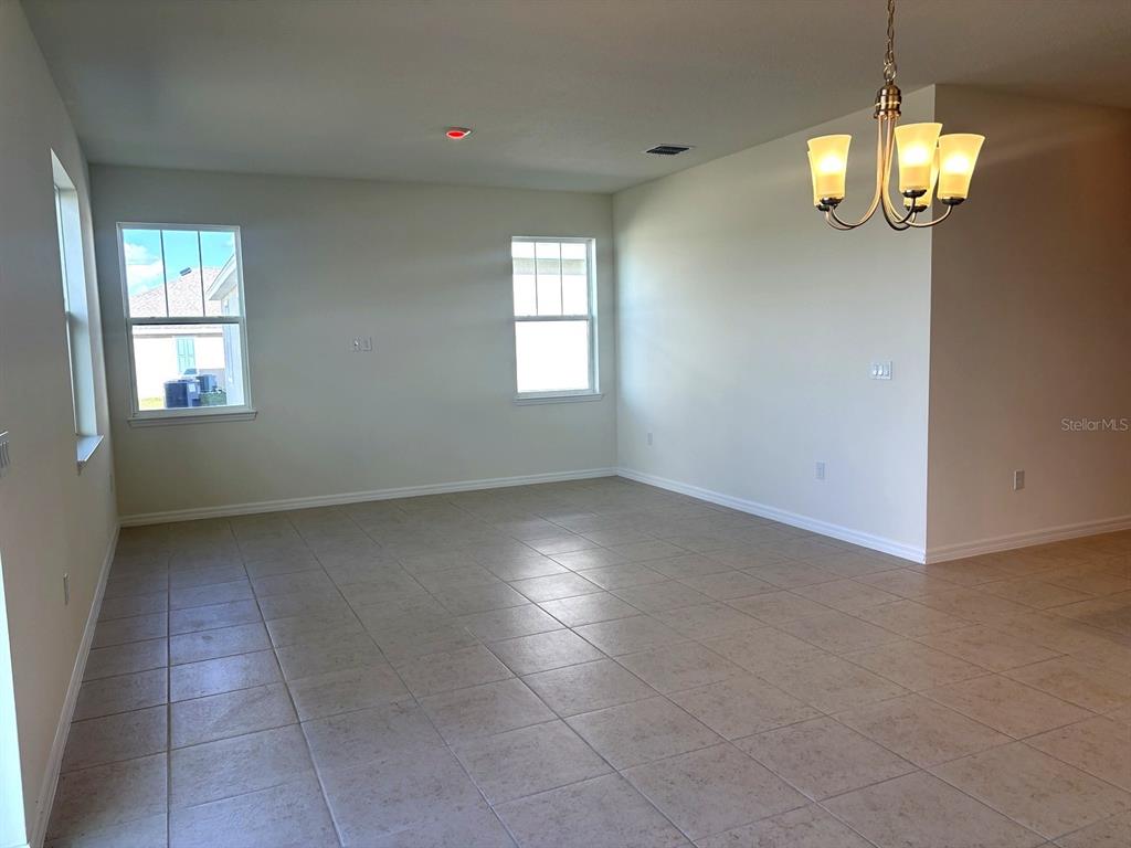 An empty room features light-colored tile flooring, white walls, two windows, and a hanging chandelier — 2363 SELENIA STREET, LAKE ALFRED, FL