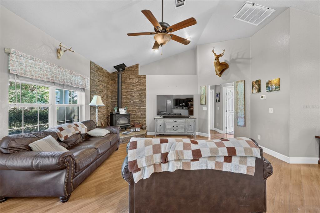 A living room features a stone corner fireplace, vaulted ceilings, and two brown leather sofas — 13930 NE 41ST TERRACE, ANTHONY, FL