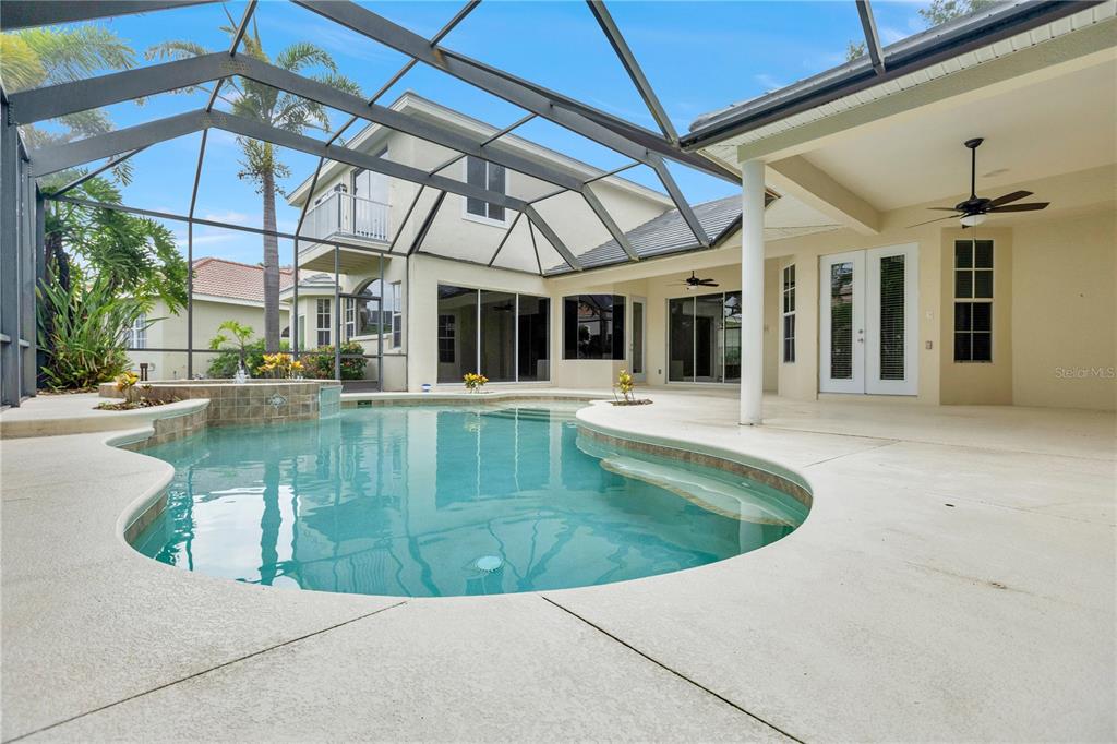 A swimming pool with a spa sits inside a screened-in patio behind a two-story house — 8018 WATERVIEW BOULEVARD, BRADENTON, FL
