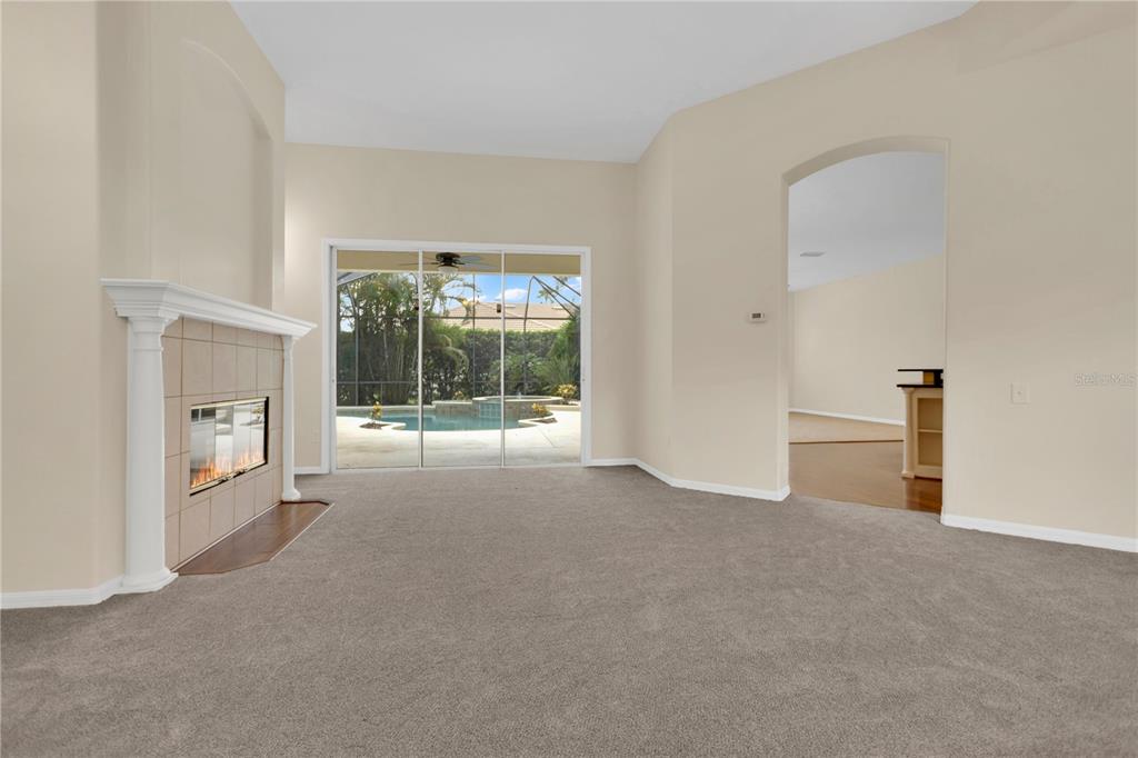 A living room with beige walls, gray carpet, a fireplace, and sliding doors to a pool — 8018 WATERVIEW BOULEVARD, BRADENTON, FL