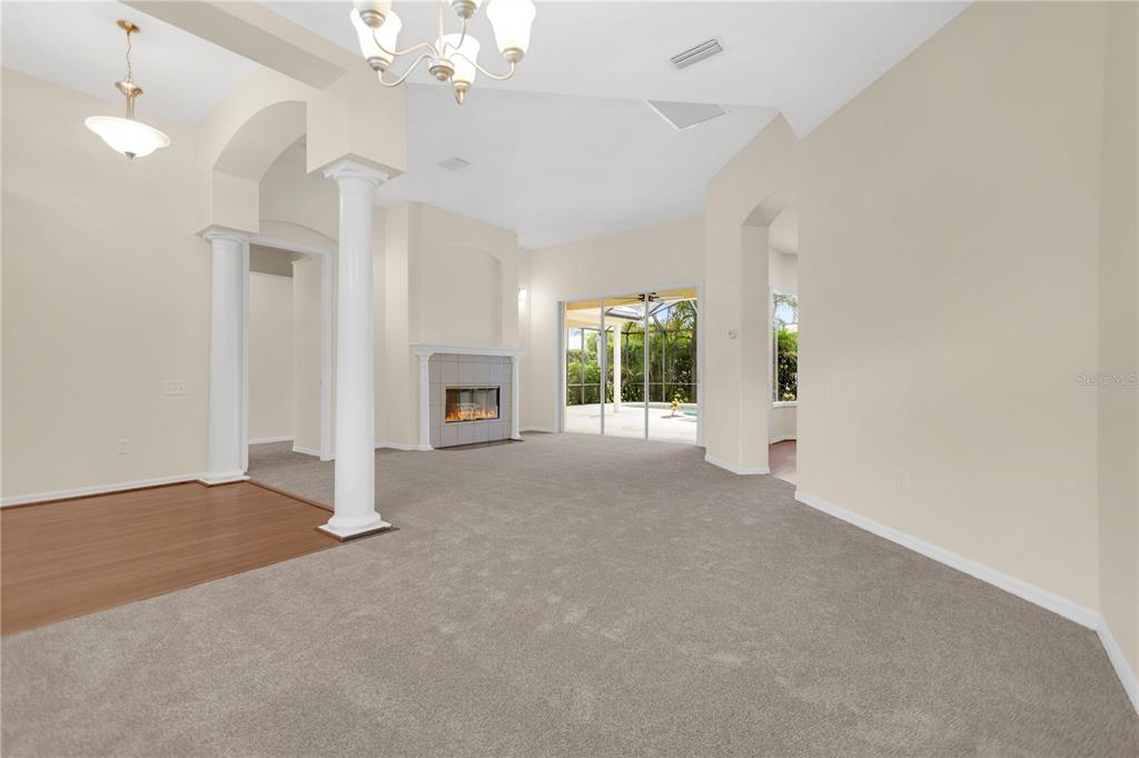 A living room with gray carpet, a fireplace, white columns, and sliding glass doors to a pool — 8018 WATERVIEW BOULEVARD, BRADENTON, FL