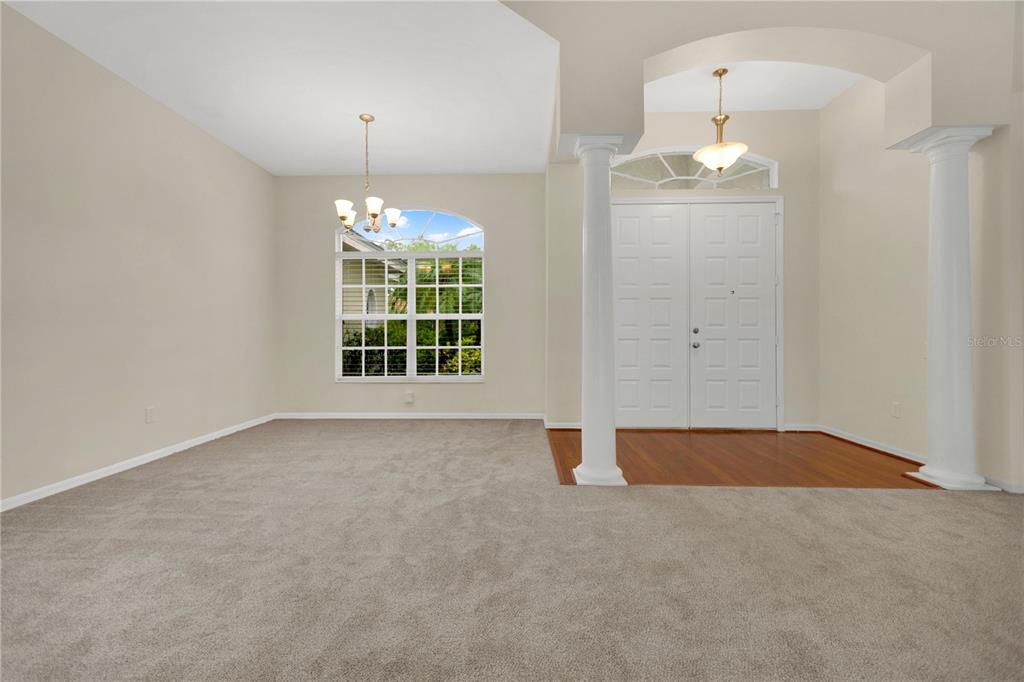 A dining room with carpeted floors, a chandelier, and an entryway with white columns — 8018 WATERVIEW BOULEVARD, BRADENTON, FL