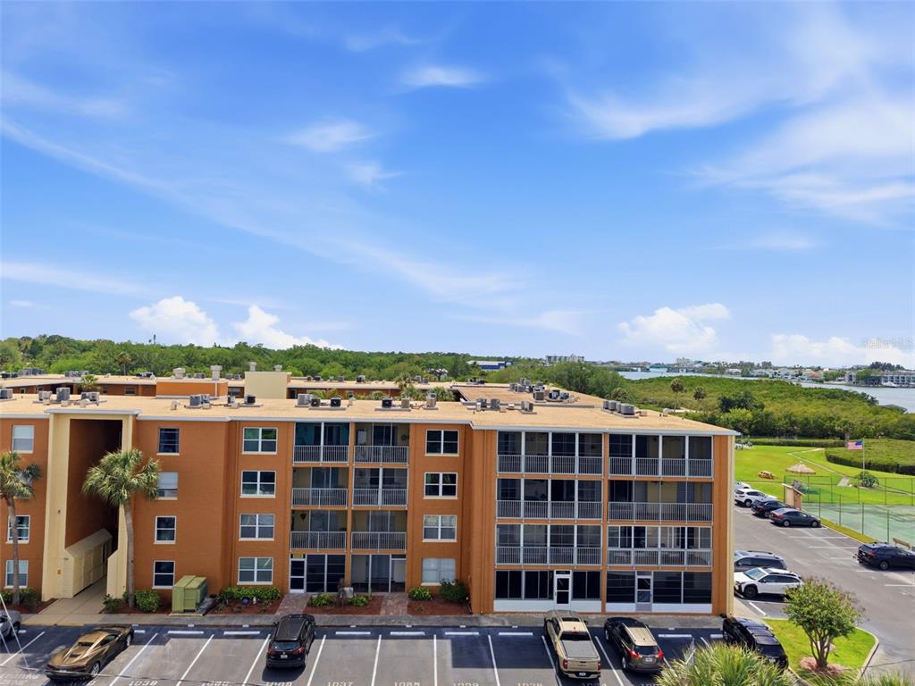 An exterior view of a multi-story apartment building with a parking lot and greenery — 12760 INDIAN ROCKS ROAD UNIT 1065, LARGO, FL