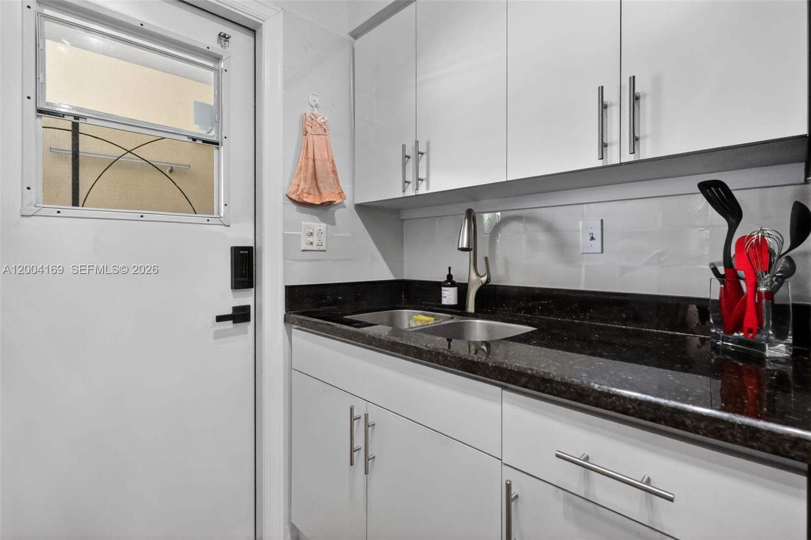 A kitchen features white cabinets, a black granite countertop, a double sink, and a door — 1820 Venice Park Dr # 102, North Miami FL 33181, NORTH MIAMI, FL