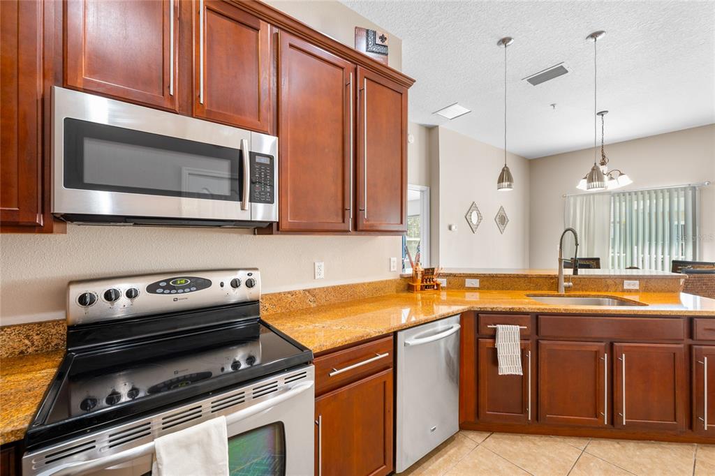 A kitchen features dark wood cabinets, granite countertops, stainless steel appliances, and tile flooring — 10235 CALA LILY TRAIL UNIT 35A, ORLANDO, FL