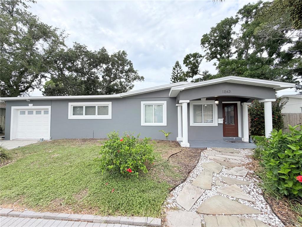 A single-story gray house features a white garage door, a stone walkway, and white columns — 1843 OKLAHOMA AVENUE NE, ST PETERSBURG, FL