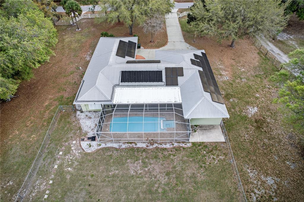 An aerial view shows a house with a metal roof, solar panels, and a screened pool — 2065 OAK BEACH BOULEVARD, SEBRING, FL
