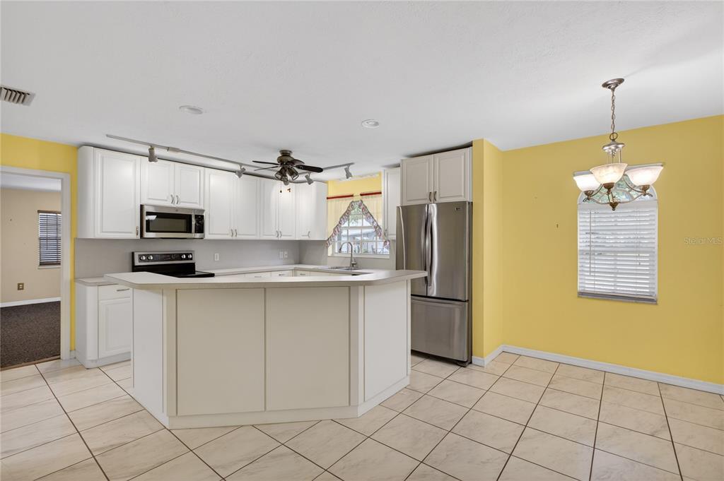 A kitchen with white cabinets, stainless steel appliances, and yellow walls over tiled flooring — 2065 OAK BEACH BOULEVARD, SEBRING, FL