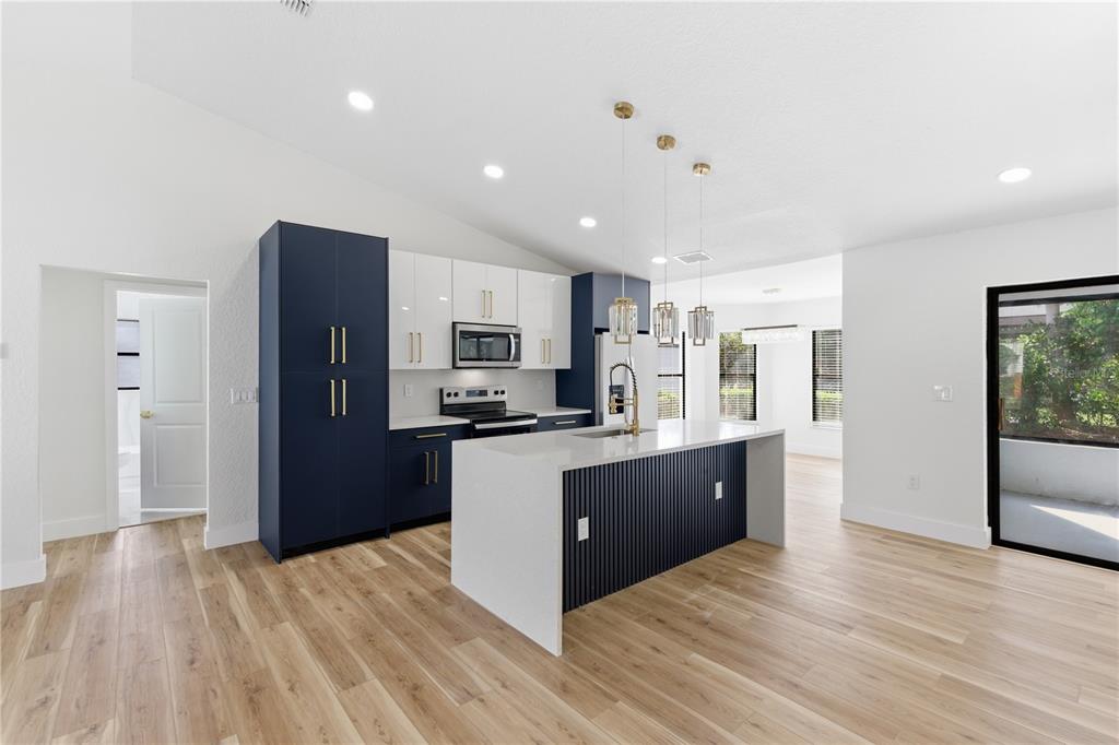 A modern kitchen features navy blue and white cabinetry, a quartz island, and light wood flooring — 1215 WATERFALL DRIVE, SPRING HILL, FL