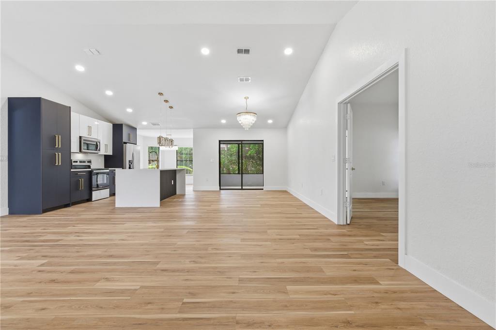 An open-concept kitchen and living area features light wood flooring, white walls, and dark cabinetry — 1215 WATERFALL DRIVE, SPRING HILL, FL